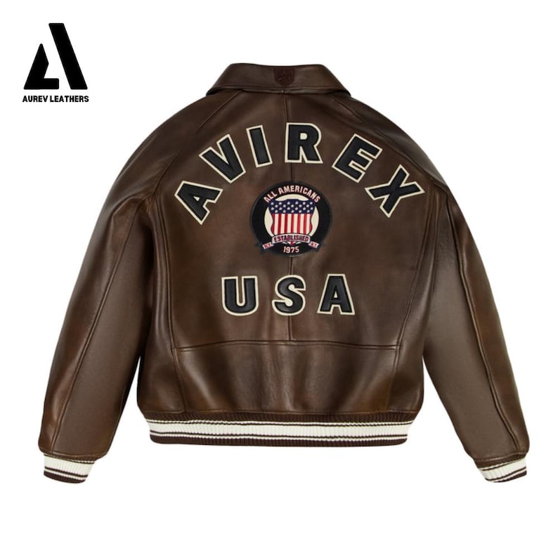 May include: Brown leather jacket with the word "AVIREX" arched across the back, along with a patch featuring the American flag and the word "USA". The jacket has a ribbed white and brown striped hem and cuffs.