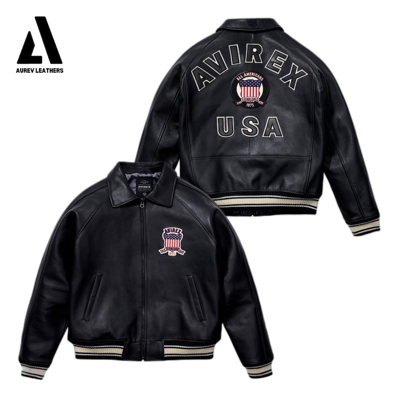 May include: Black leather jacket with a classic collar and a zip-up front. The jacket features a patch on the chest and the back with the text "AVIREX" and "USA". The jacket has white and cream-colored striped cuffs and hem. The Aurev Leathers logo is in the top left corner.