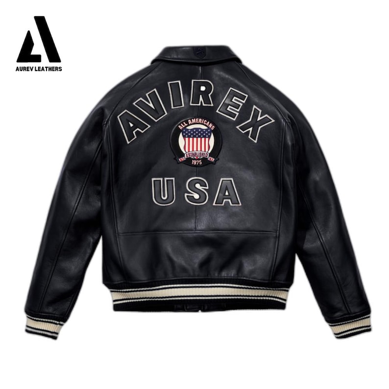May include: Black leather jacket with white and cream striped cuffs and collar. The back features the word "AVIREX" in white lettering above a patch with the American flag and the word "USA". The jacket is a classic bomber style.