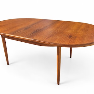 May include: An oval wooden dining table with a warm brown grain pattern and a smooth surface. The table features four tapered legs that extend outwards from the centre, supporting the rounded top which includes a visible seam for an extension leaf.