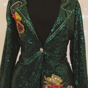 May include: Emerald green sequined blazer with gold trim and decorative embroidery. The blazer features a single button closure and two front pockets. The embroidery includes a teacup, flowers, and a key. The blazer is displayed on a mannequin.