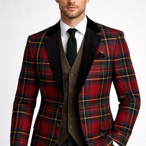 Può includere: Un blazer a quadri rossi, verdi e gialli con colletto in velluto nero, indossato sopra un gilet marrone e una camicia bianca. L'ensemble è completato da una cravatta verde scuro e pantaloni neri. Un fazzoletto da taschino è visibile nella tasca del blazer.