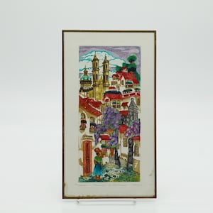May include: Framed artwork depicting a European town scene with red-roofed buildings, a church, and a person carrying a basket. The artwork features a color palette of red, purple, green, and yellow. The text at the bottom reads "Dominique in the France".