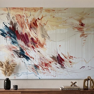 May include: Abstract canvas art with a cream background and vertical white lines. The artwork features dynamic brushstrokes in shades of red, blue, and beige. A black vase with dried flowers and decorative items are on a wooden surface.
