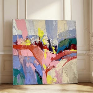 May include: A large, square abstract painting with a vibrant color palette. The artwork features broad brushstrokes in shades of pink, yellow, blue, red, and green. The painting is leaning against a white wall with a wooden floor.