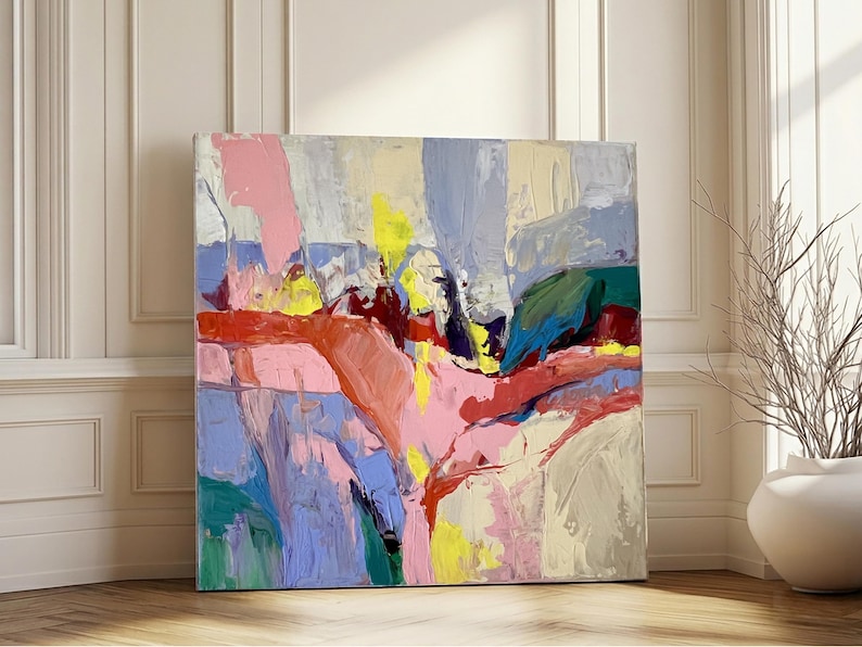 May include: A large, square abstract painting with a vibrant colour palette. The artwork features broad brushstrokes in shades of pink, yellow, blue, red, and green. The painting is leaning against a white wall with a wooden floor.