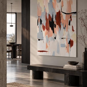 May include: A large rectangular canvas painting featuring abstract brushstrokes in shades of terracotta, soft peach, light blue, and black against a white background, displayed on a wall above a dark wooden bench with books and a bowl.