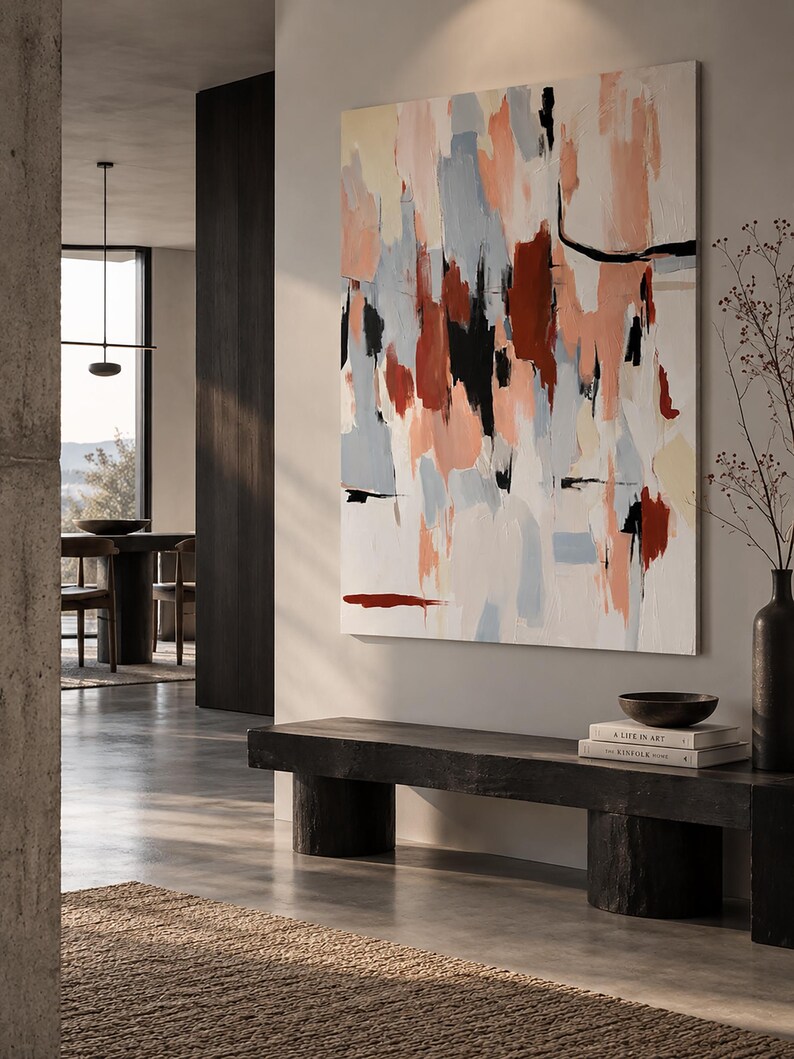 May include: A large rectangular canvas painting featuring abstract brushstrokes in shades of terracotta, soft peach, light blue, and black against a white background, displayed on a wall above a dark wooden bench with books and a bowl.