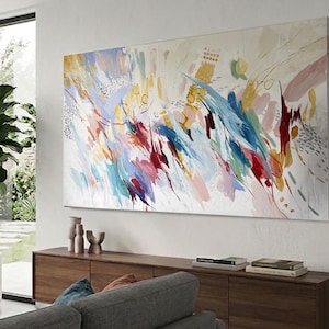 May include: Large abstract painting with a white background and colorful brushstrokes in shades of blue, red, yellow, and pink. The artwork is mounted on a white wall above a wooden cabinet.