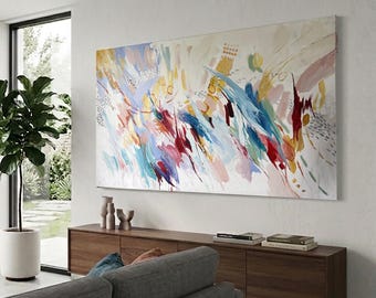 May include: Large abstract painting with a white background and colorful brushstrokes in shades of blue, red, yellow, and pink. The artwork is mounted on a white wall above a wooden cabinet.
