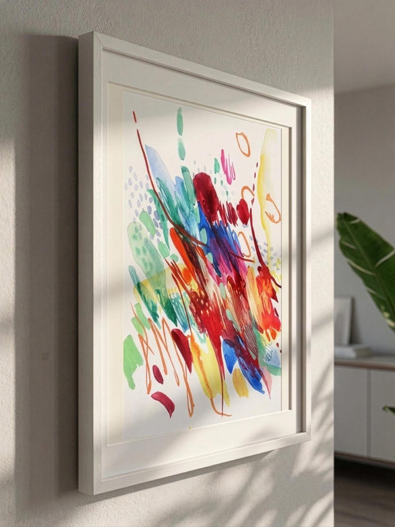 May include: A framed wall art piece featuring an abstract watercolor painting on a white background. The artwork displays vibrant, energetic brushstrokes in shades of red, blue, yellow, and green, with scattered dots and thin, curved line details.