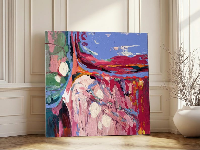 May include: Abstract square canvas art with a vibrant color palette. The artwork features a blend of pink, red, blue, and green hues, with white circular accents. The painting is displayed against a white wall and wooden floor.