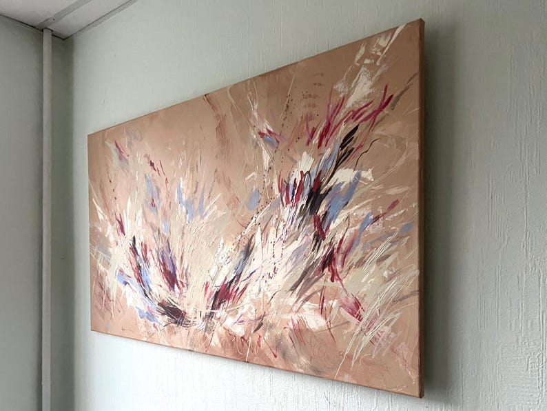 May include: Abstract painting on canvas with a beige background and dynamic brushstrokes in white, red, and blue. The artwork is mounted on a wooden frame and leans against a light gray wall.