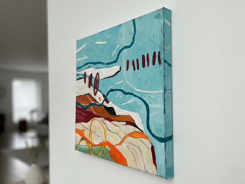 May include: Square abstract painting with a textured surface. The artwork features a light blue background with white, orange, and dark red shapes. The painting is mounted on a canvas frame and displayed on a white wall.