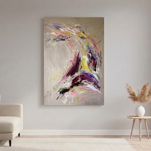 May include: Abstract painting with a beige background and a dynamic swirl of colors. The artwork features strokes of purple, yellow, pink, and green, creating a sense of movement and energy. The painting is displayed on a wall above a beige sofa.