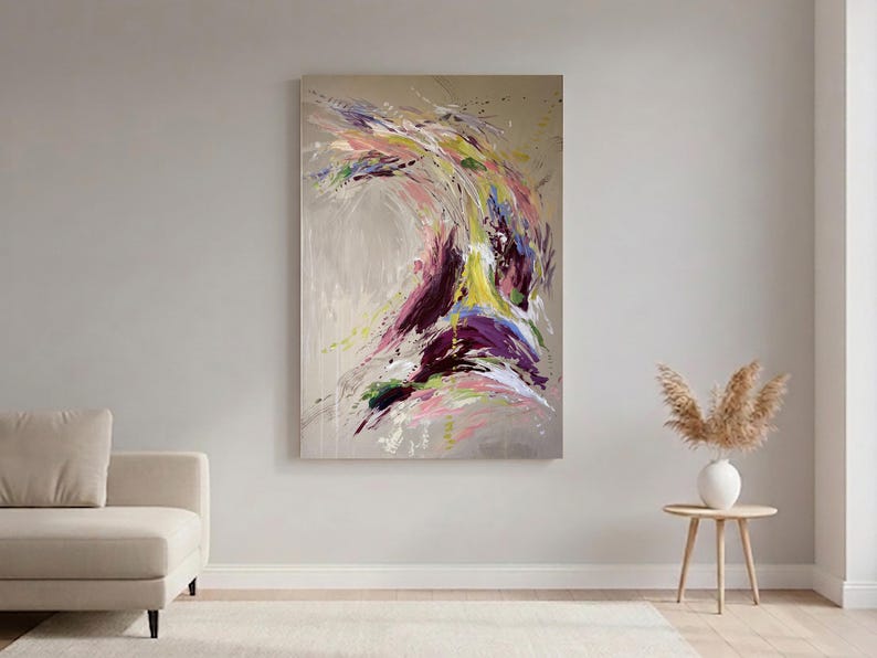 May include: Abstract painting with a beige background and a dynamic swirl of colors. The artwork features strokes of purple, yellow, pink, and green, creating a sense of movement and energy. The painting is displayed on a wall above a beige sofa.