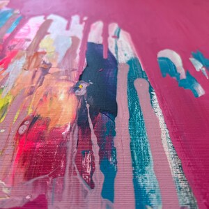 May include: Abstract art piece with a vibrant color palette. The artwork features a bright pink background with streaks of teal, white, yellow, and dark blue paint. The paint appears to be dripping down the canvas, creating a dynamic visual effect.