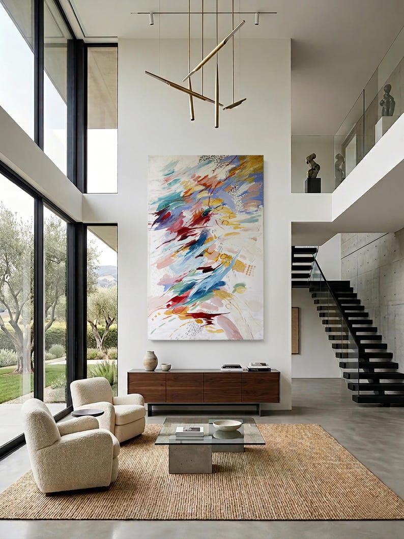 Puede incluir: Sal&oacute;n moderno con grandes ventanales, dos sillones color crema y una alfombra rectangular tejida. Una gran pintura abstracta con pinceladas rojas, azules y amarillas cuelga sobre un mueble de madera oscura. Una mesa de centro de cristal en el centro.
