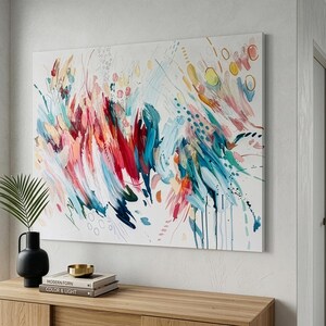 Pode incluir: Uma grande pintura retangular em tela apresentando uma composi&ccedil;&atilde;o abstrata de pinceladas energ&eacute;ticas em tons vibrantes de vermelho, azul-petr&oacute;leo, azul, amarelo e rosa sobre um fundo branco, com pontos espalhados e padr&otilde;es de linhas circulares.