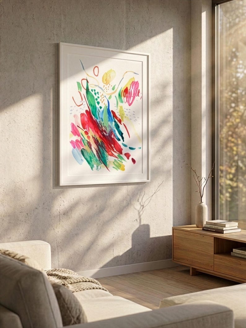 May include: A framed vertical wall art print featuring an abstract watercolor composition with vibrant brushstrokes in red, green, blue, and yellow on a white background, displayed in a simple white frame mounted on a textured concrete wall.