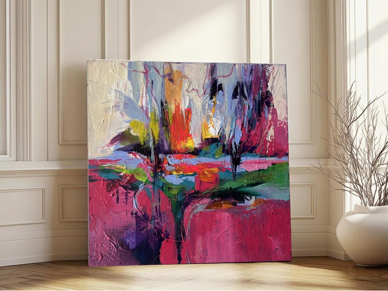 May include: An abstract painting with a vibrant color palette. The artwork features bold brushstrokes in shades of pink, red, blue, green, and yellow. The canvas is square and leans against a white wall and wooden floor.