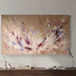 May include: Abstract painting on a beige canvas. The artwork features dynamic brushstrokes in white, red, and blue, creating a sense of movement. The painting is displayed above a wooden cabinet with decorative items.
