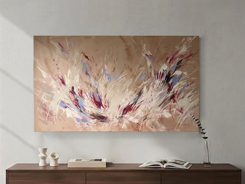 May include: Abstract painting on a beige canvas. The artwork features dynamic brushstrokes in white, red, and blue, creating a sense of movement. The painting is displayed above a wooden cabinet with decorative items.