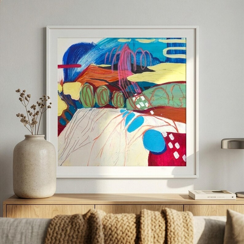 May include: A square framed abstract painting featuring vibrant layers of blue, red, yellow, and green. The composition includes bold brushstrokes, swirling pink lines, and solid geometric shapes, creating a dynamic visual texture within a white frame.