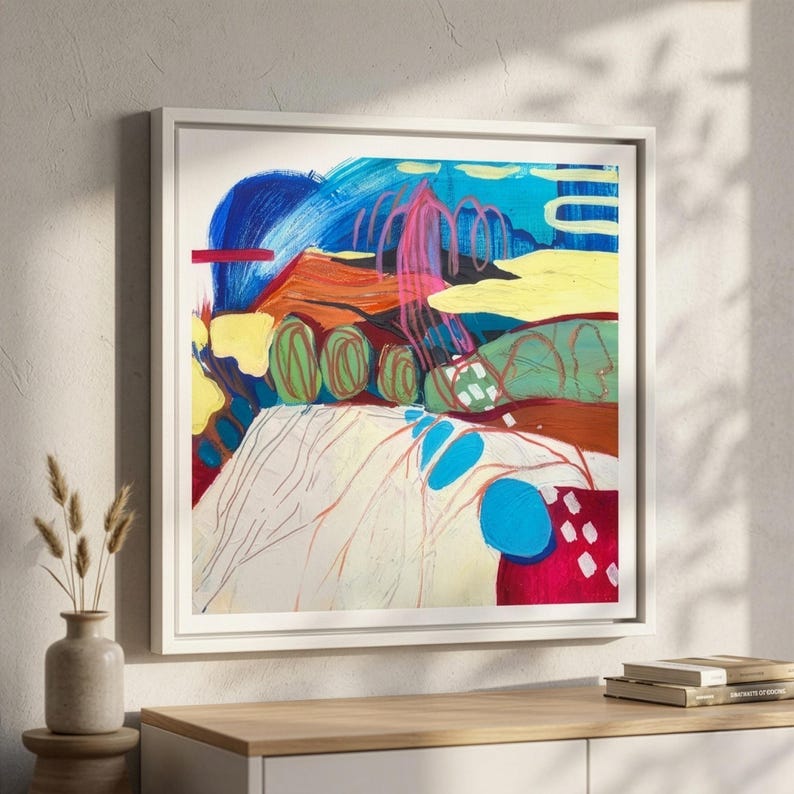 May include: A square framed abstract painting featuring bold, expressive brushstrokes in vibrant shades of blue, yellow, red, and green. The composition includes layered shapes, swirling lines, and textured colour blocks, all contained within a simple white frame.
