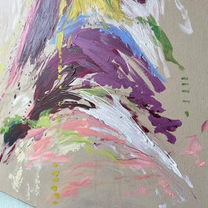 May include: Abstract painting on canvas with a neutral background. The artwork features bold brushstrokes in shades of purple, pink, white, yellow, blue, and green. The paint appears textured and layered, creating a dynamic and expressive composition.