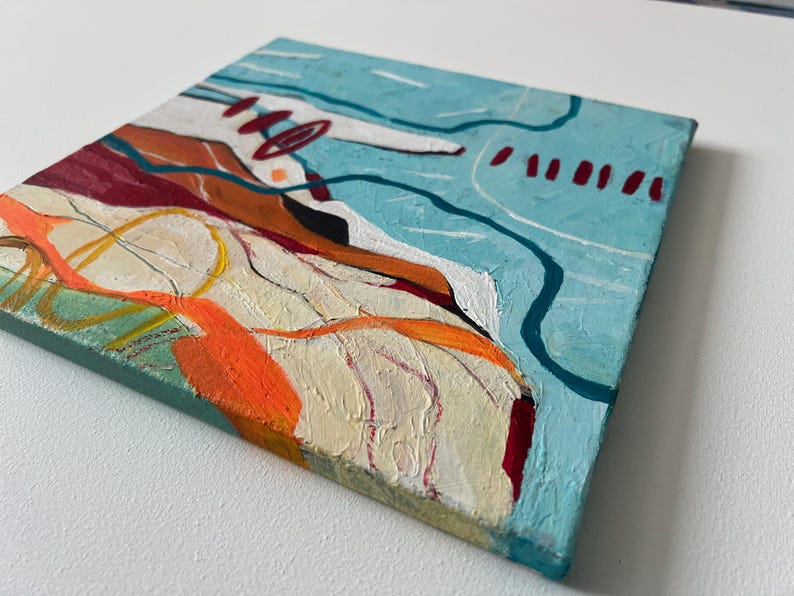 May include: Abstract painting on a square canvas. The artwork features a textured surface with a palette of colors including light blue, orange, red, and white. The composition includes lines and shapes, creating a modern art piece.
