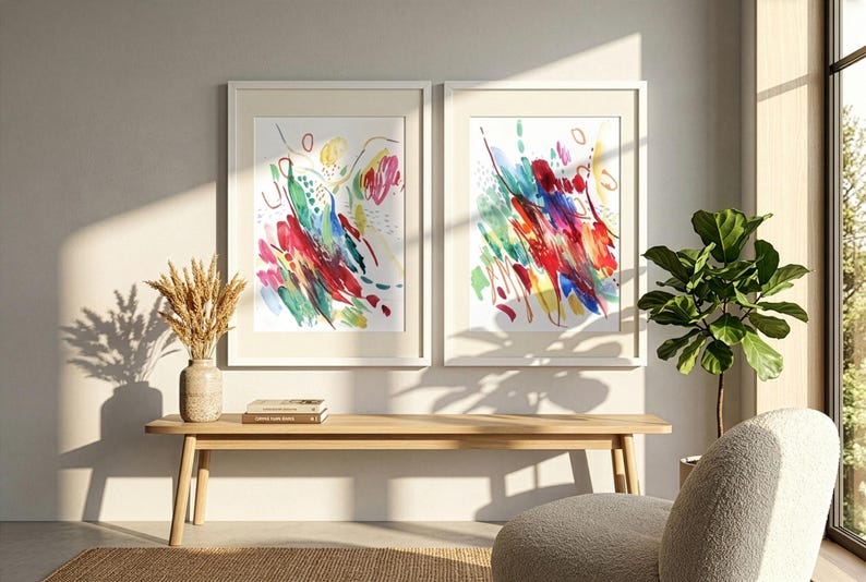 May include: Two framed vertical wall art prints featuring abstract watercolor brushstrokes in vibrant shades of red, blue, yellow, and green on a white background, displayed side by side in light-colored wooden frames on a plain wall.