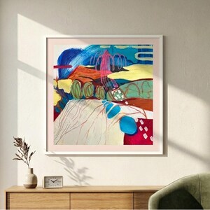 May include: A square abstract painting in a white frame featuring bold brushstrokes of blue, red, yellow, and green. The composition includes layered shapes, swirling lines, and textured colour blocks that create a dynamic, multi-coloured visual landscape.