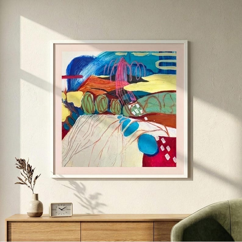 May include: A square abstract painting in a white frame featuring bold brushstrokes of blue, red, yellow, and green. The composition includes layered shapes, swirling lines, and textured colour blocks that create a dynamic, multi-coloured visual landscape.