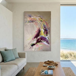 May include: Abstract painting with a dynamic composition of colors. The artwork features a blend of purple, yellow, pink, and white hues against a neutral background. The painting is displayed in a modern living room setting.