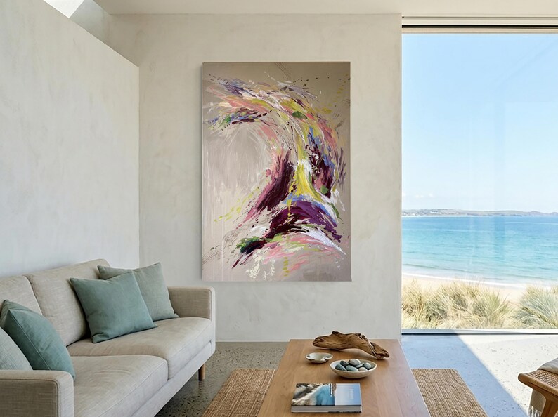 May include: Abstract painting with a dynamic composition of colors. The artwork features a blend of purple, yellow, pink, and white hues against a neutral background. The painting is displayed in a modern living room setting.
