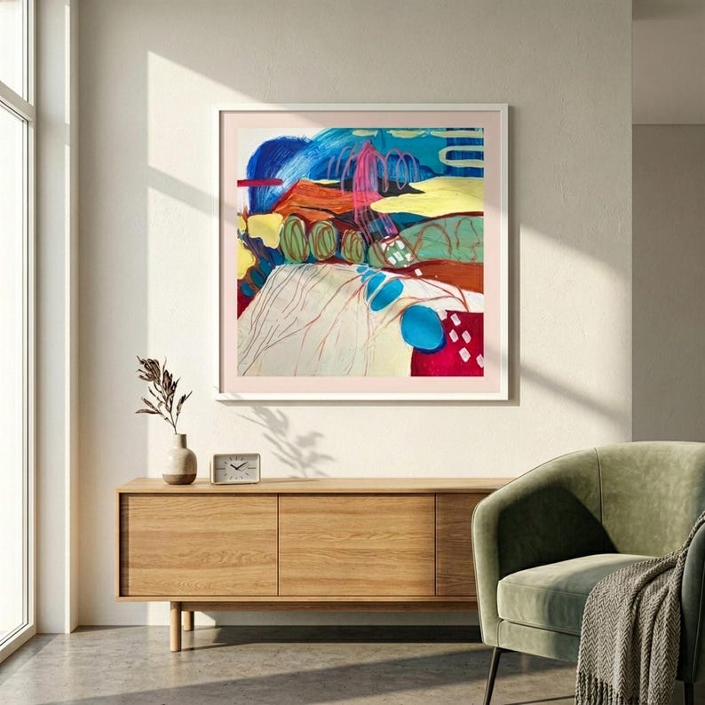 May include: A square framed abstract painting featuring vibrant layers of blue, red, yellow, and green. The composition includes bold brushstrokes, swirling lines, and solid colour blocks, presented in a light-coloured frame on a wall.