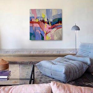 May include: An abstract painting in shades of pink, yellow, and blue adorns a white wall. The modern living room includes a light blue lounge chair and ottoman, a glass coffee table, and a floor lamp. The room has a contemporary feel.