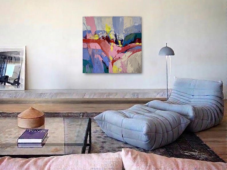 May include: An abstract painting in shades of pink, yellow, and blue adorns a white wall. The modern living room includes a light blue lounge chair and ottoman, a glass coffee table, and a floor lamp. The room has a contemporary feel.