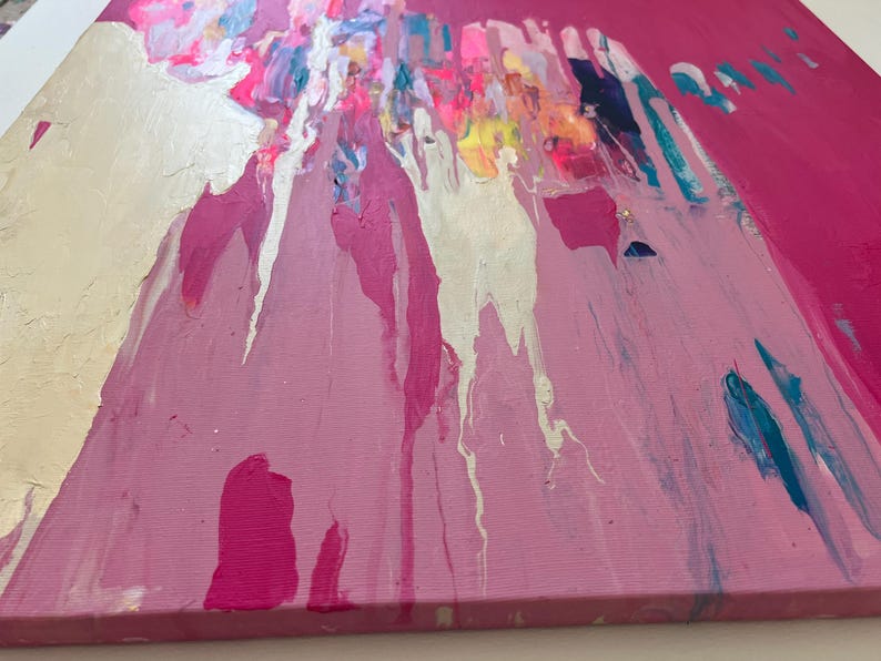 May include: Abstract painting on canvas with a vibrant pink background. Silver, white, and various shades of pink and blue paint drip down from the top, creating a dynamic and textured effect. The artwork has a modern and expressive style.