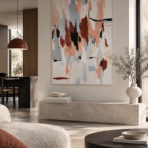 May include: A large rectangular canvas painting featuring abstract brushstrokes in shades of peach, light blue, cream, deep red, and black. The artwork is displayed on a wall above a long, low, textured stone bench in a neutral-toned room.
