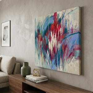 May include: Abstract art painting with bold brushstrokes in red, blue, and white hues. The artwork is mounted on a wall, adding a vibrant focal point to the room's decor. The painting is displayed above a wooden cabinet.