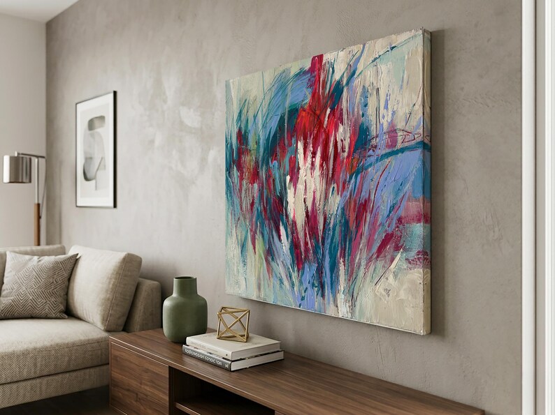 May include: Abstract art painting with bold brushstrokes in red, blue, and white hues. The artwork is mounted on a wall, adding a vibrant focal point to the room's decor. The painting is displayed above a wooden cabinet.