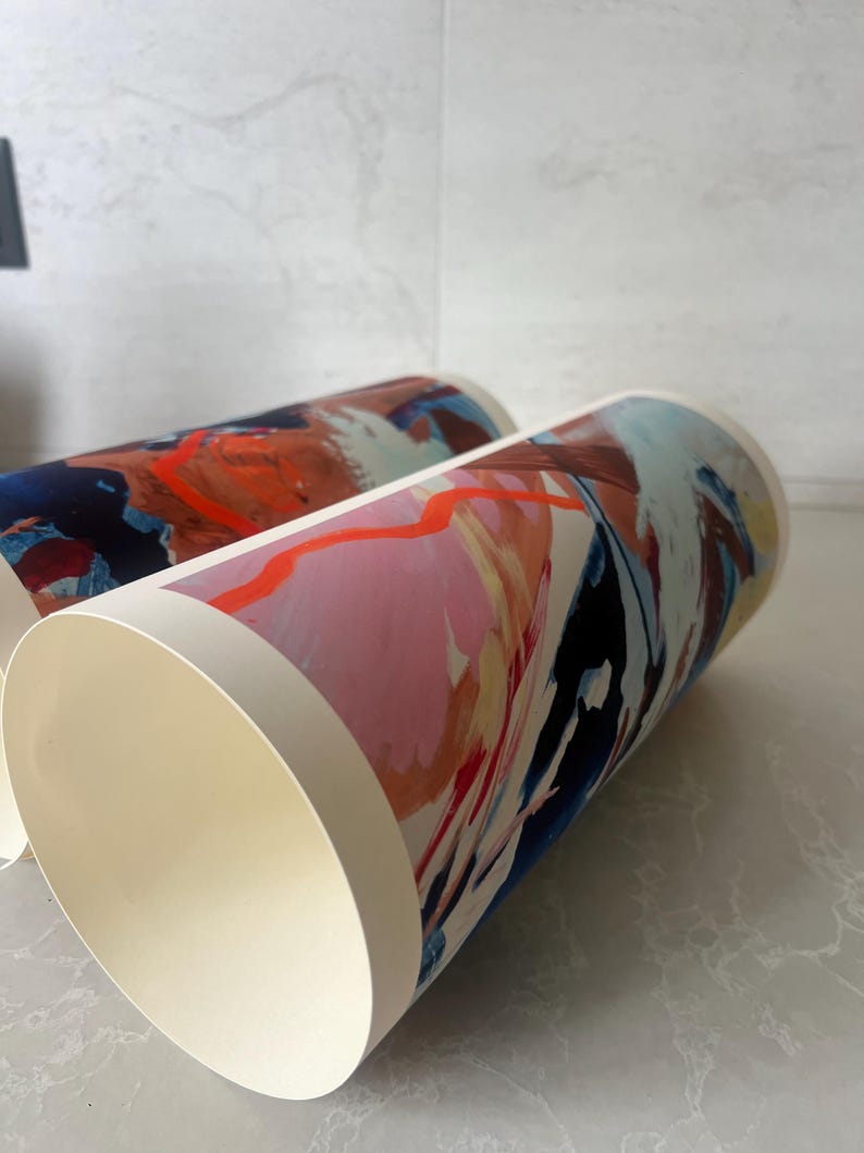 Puede incluir: Dos rollos de papel cil&iacute;ndricos con impresiones de arte abstracto. Los dise&ntilde;os muestran una paleta de colores vibrantes de naranja brillante, rosa suave, azul marino profundo y crema. Los patrones de pinceladas est&aacute;n superpuestos.