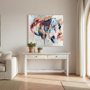 May include: Abstract art piece with a profile in shades of blue, red, and orange. The artwork hangs above a white wooden console table with two drawers. Two potted plants sit on the table. The room has a neutral color palette.