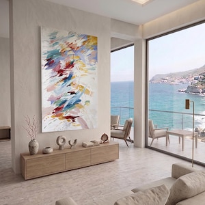 Puede incluir: Una pintura abstracta con fondo blanco y pinceladas coloridas en tonos azules, rojos, amarillos y rosas. La obra cuelga sobre un mueble de madera con objetos decorativos. La habitaci&oacute;n ofrece vistas al mar.