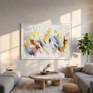 May include: A large rectangular framed wall art piece featuring an abstract composition of energetic brushstrokes in shades of yellow, blue, brown, and lavender on a white background, displayed in a white frame on a light grey wall.