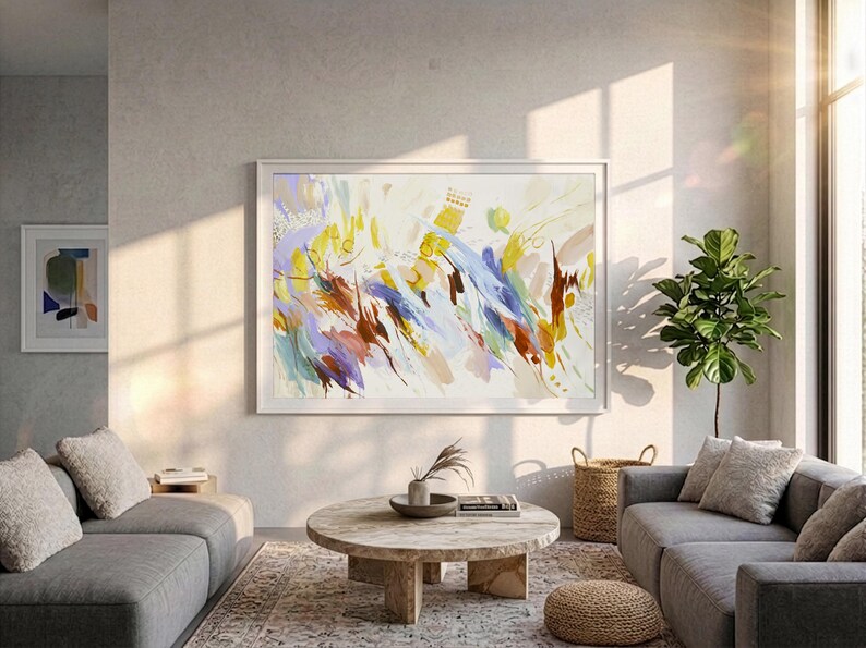 May include: A large rectangular framed wall art piece featuring an abstract composition of energetic brushstrokes in shades of yellow, blue, brown, and lavender on a white background, displayed in a white frame on a light grey wall.