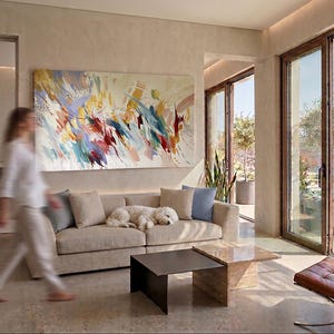 Puede incluir: Sal&oacute;n moderno con una gran pintura abstracta sobre un sof&aacute; beige. Un perro blanco descansa en el sof&aacute;. Dos mesas de centro cuadradas y una silla de cuero marr&oacute;n est&aacute;n frente a una gran ventana con vista al mar.