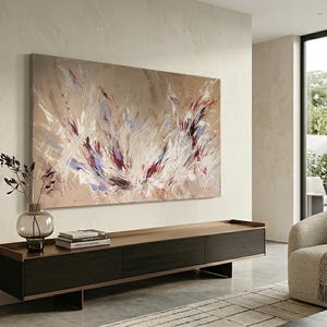 May include: Large abstract painting with beige, white, red, and blue brushstrokes. The artwork hangs above a dark wood and metal console table. A glass vase with decorative branches sits on the table, alongside books. A modern living room setting.